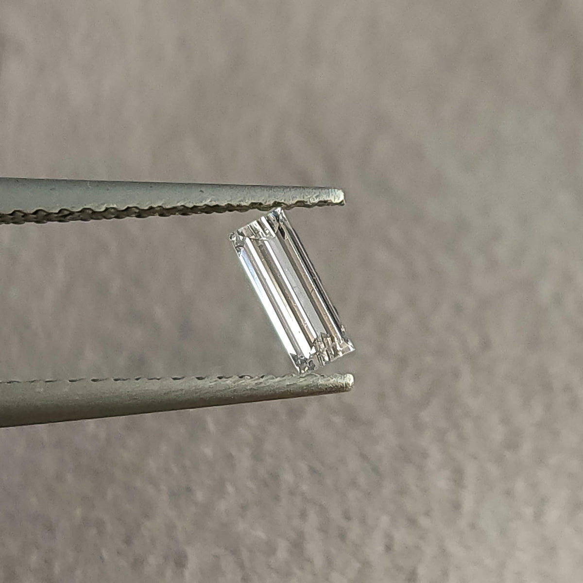Baguette diamond in tweezers tilted slightly, with a different pattern of pale and dark step-facet reflections.