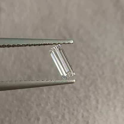 Baguette diamond in tweezers tilted slightly, with a different pattern of pale and dark step-facet reflections.