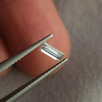 Baguette diamond tilted between tweezers near a finger, showing the outline and changing linear reflections.