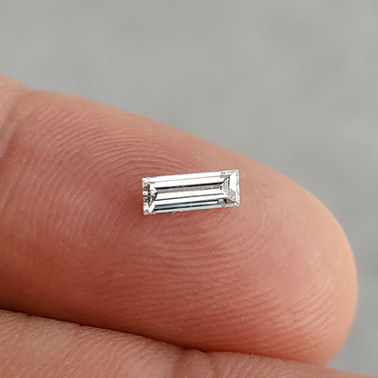 Face-up rectangular baguette diamond resting on a fingertip, with long step facets visible.