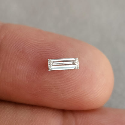 Alternate face-up fingertip view of the baguette diamond, showing bright parallel reflections.