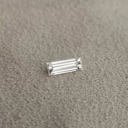 Baguette diamond lying face-up on a gray textured surface, showing its slim rectangular outline.