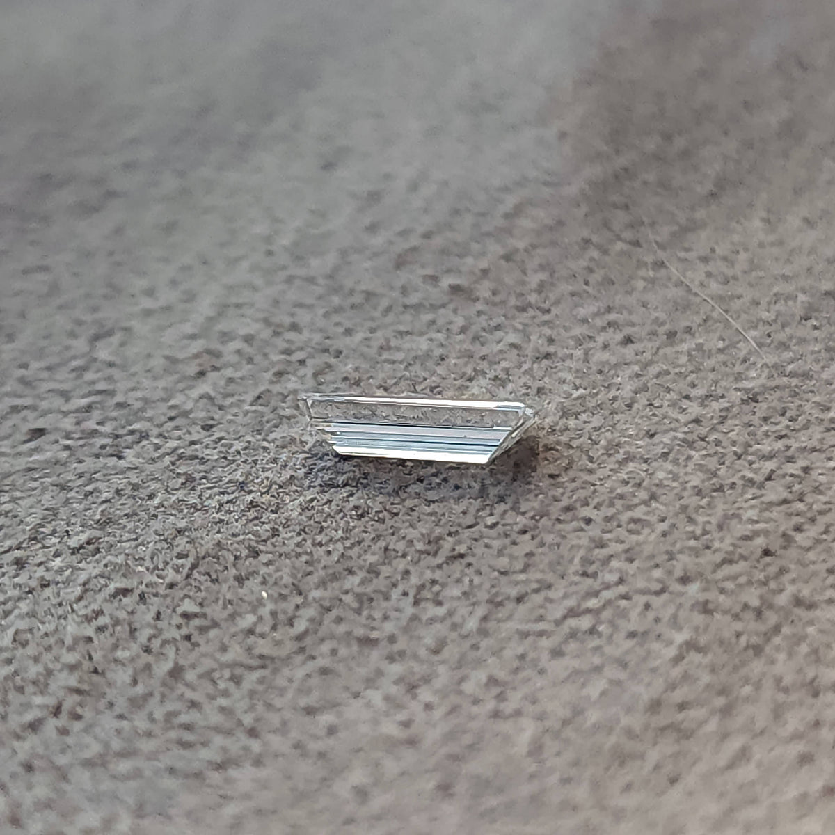 Low side-profile view of the baguette diamond on a gray textured surface, showing its shallow height.
