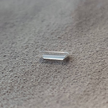 Low side-profile view of the baguette diamond on a gray textured surface, showing its shallow height.