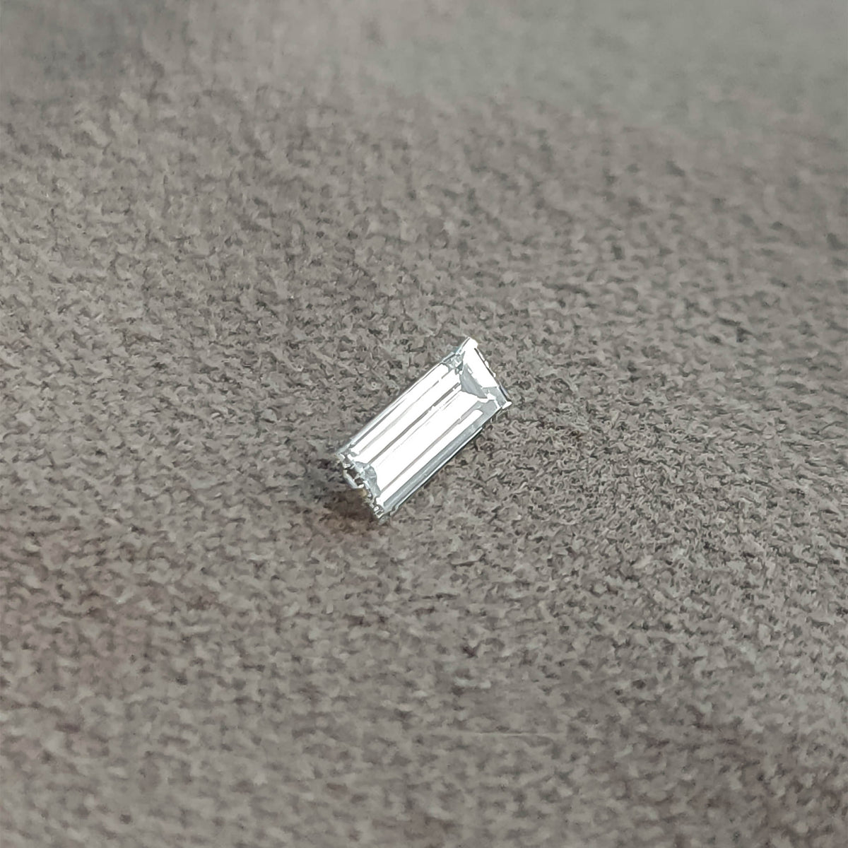 Baguette diamond resting diagonally on a gray surface, showing a different bright face-up reflection.
