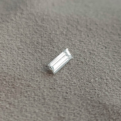 Baguette diamond resting diagonally on a gray surface, showing a different bright face-up reflection.
