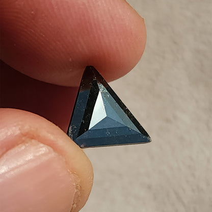 Triangular rose cut gemstone held between fingertips showing dark body color with internal speckled inclusions.