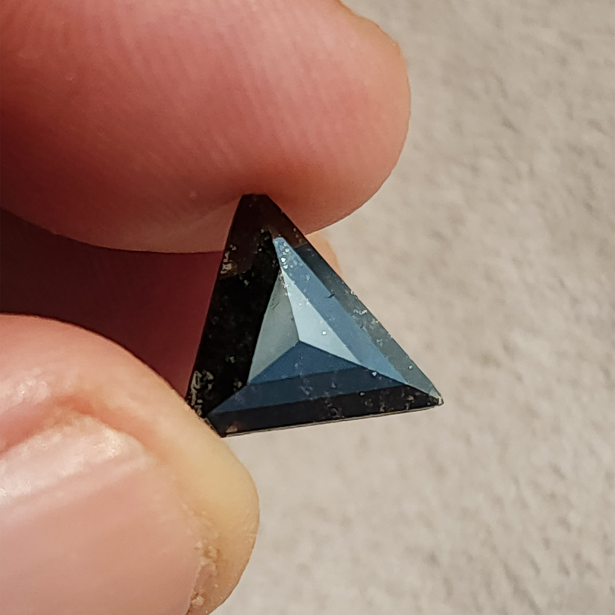 Slightly tilted face-up view of a triangular rose cut stone held between fingers displaying surface luster.