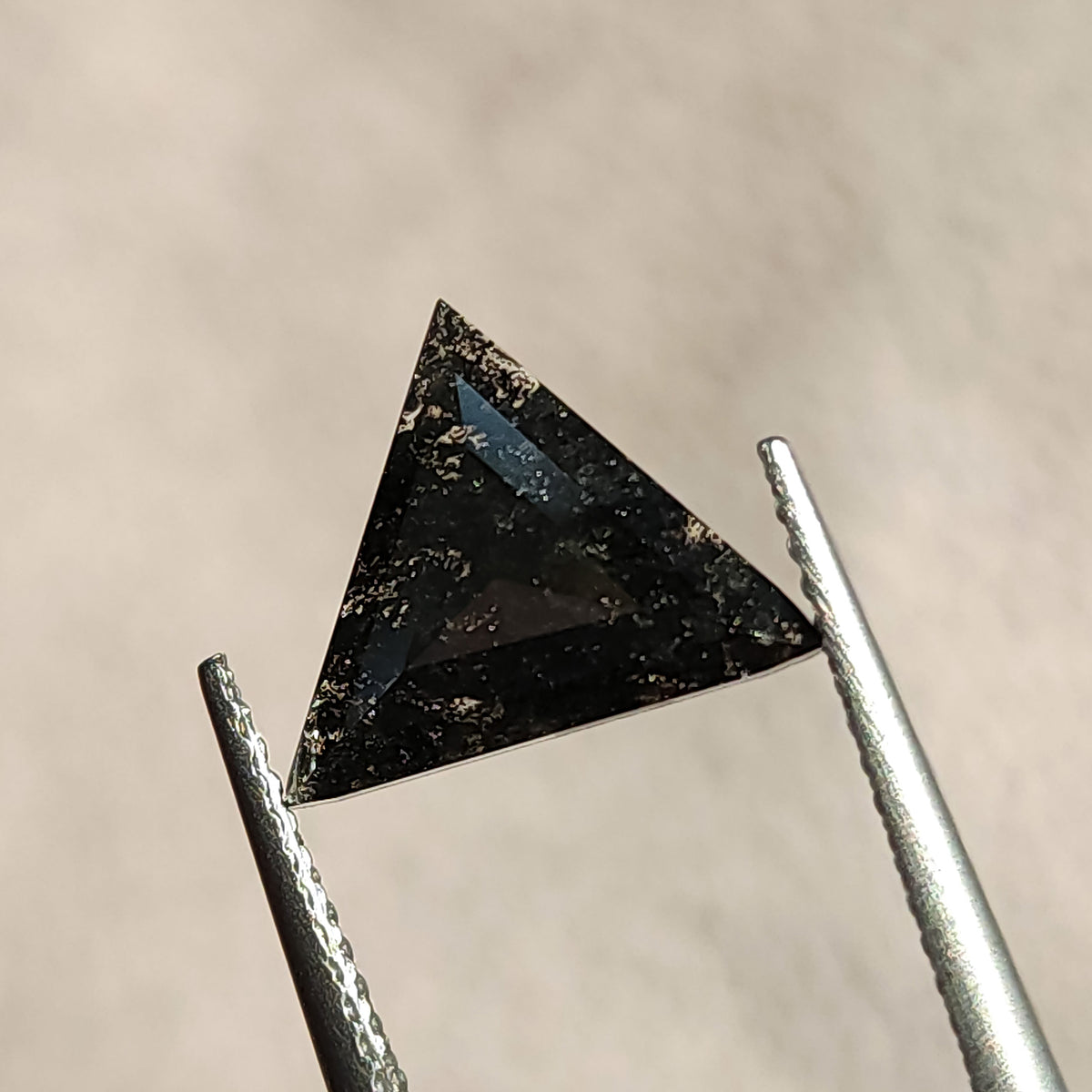 Triangular rose cut gemstone held in tweezers catching light across its dark surface.