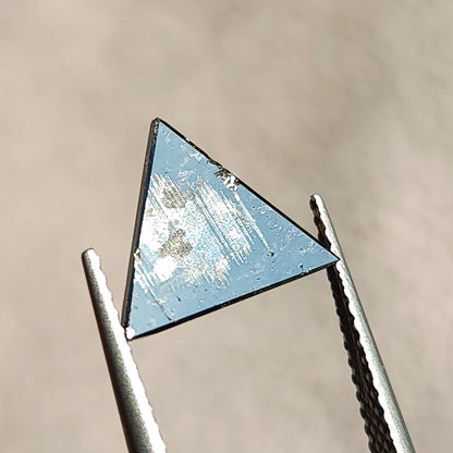 Flat back side of a triangular rose cut gemstone held in tweezers showing flat surface reflection.