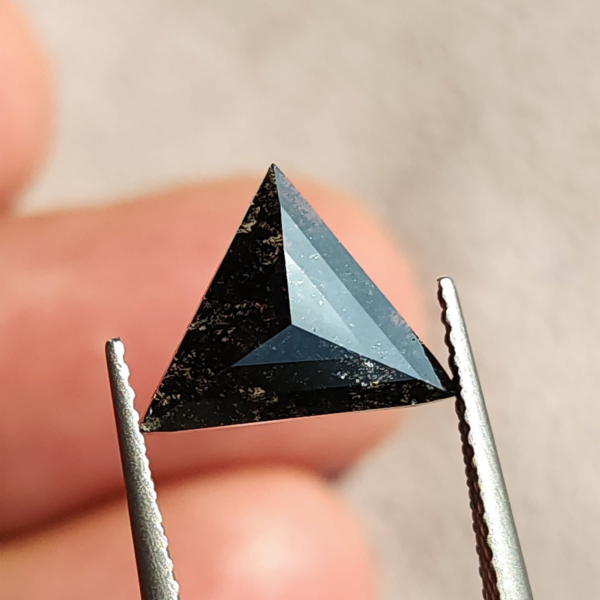 Angled view in tweezers of a triangular rose cut stone showing bright surface reflections.