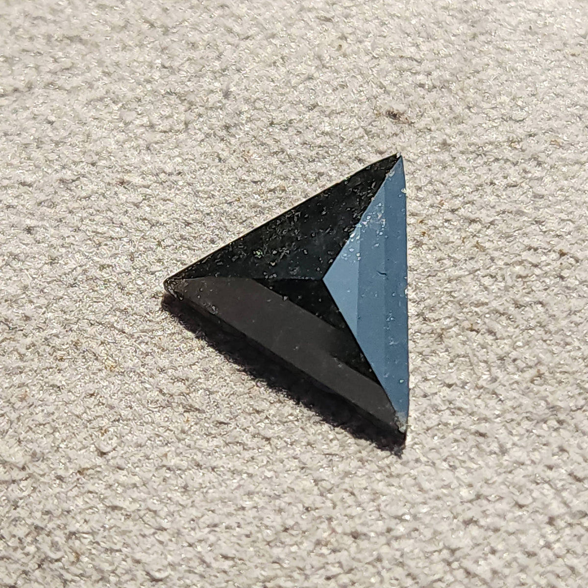 Loose triangular rose cut stone resting flat on a beige fabric background.