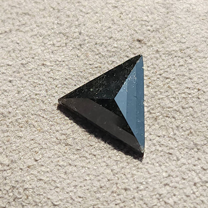 Loose triangular rose cut stone resting flat on a beige fabric background.