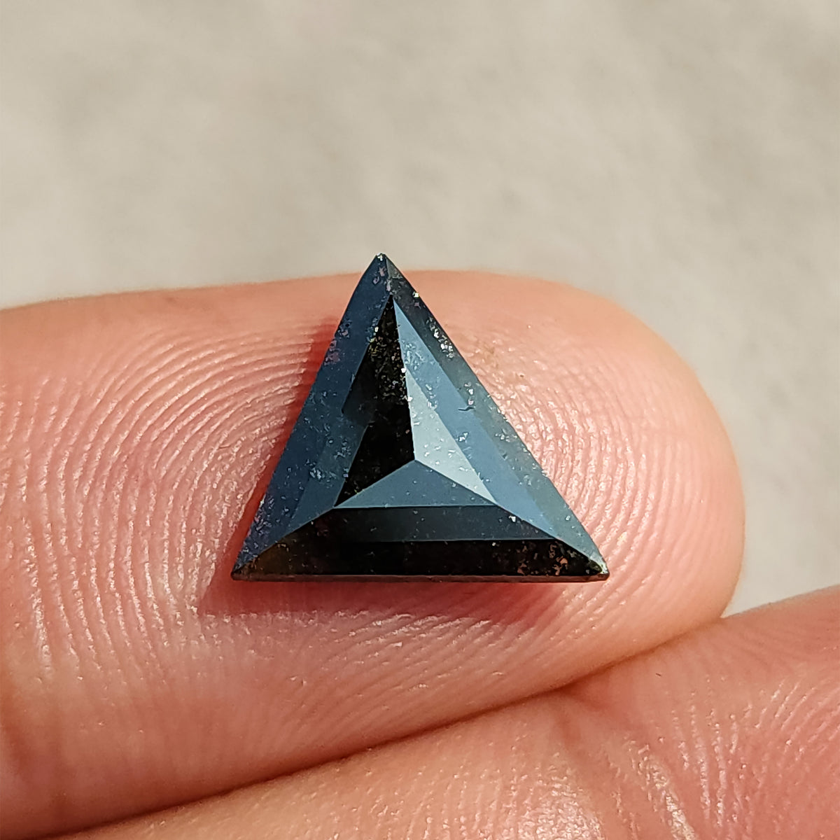 Triangular rose cut dark gemstone resting flat on a human finger for scale reference.