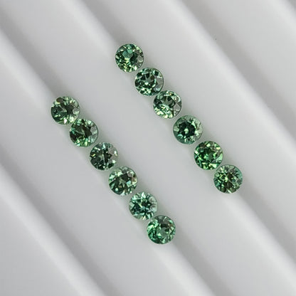 Mint-green round lab-grown sapphire stock arranged table-up in two rows on a white grooved tray.