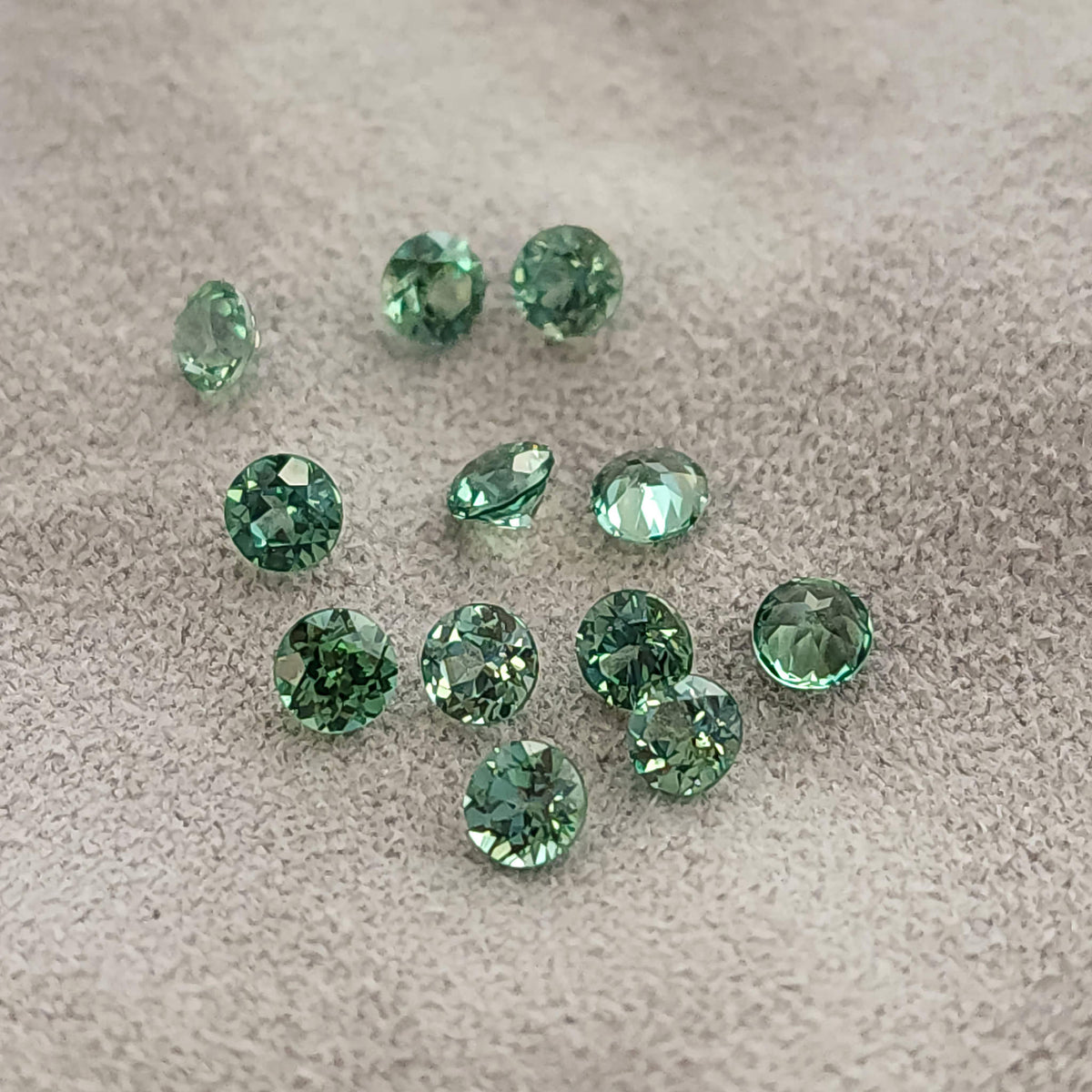 Loose mint-green round lab-grown sapphires on gray fabric in mixed crown, pavilion and side orientations.