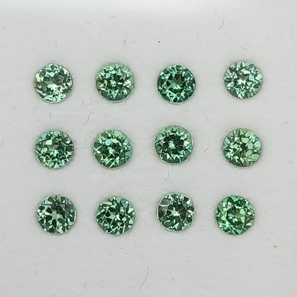 Round mint-green lab-grown sapphires arranged table-up in a grid on a white display surface.