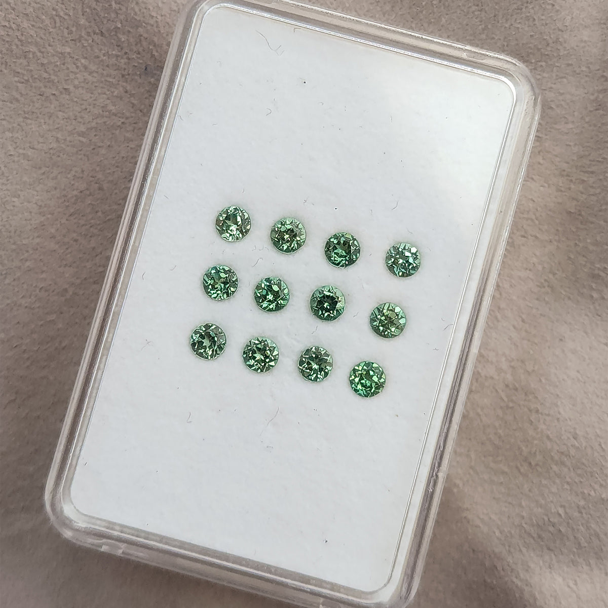 Clear display case viewed at an angle with mint-green round lab-grown sapphires arranged table-up.