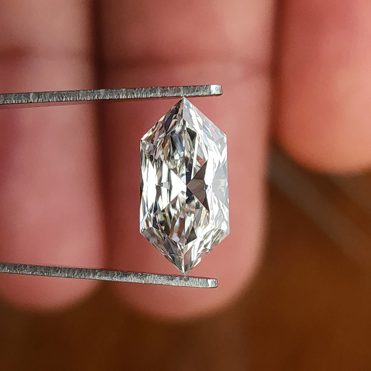 Colorless Dutch marquise hexagon cut gem gripped vertically in tweezers against fingers.