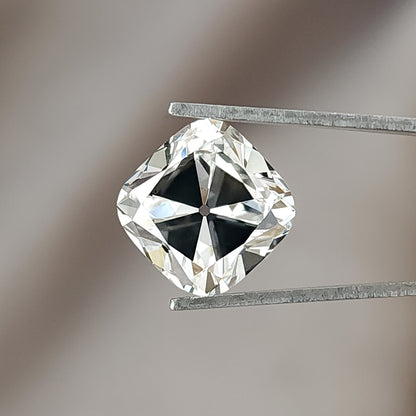 Face-up view of a colorless square cushion cut diamond held in metal tweezers against a neutral backdrop.