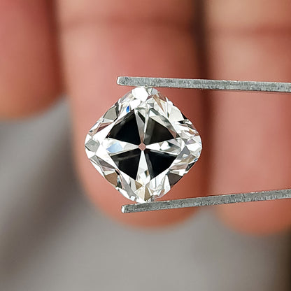 Square cushion cut colorless stone held in tweezers over fingers, showing table and facet reflections.