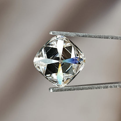 Colorless square cushion diamond in tweezers showing faint rainbow facet fire under direct light.