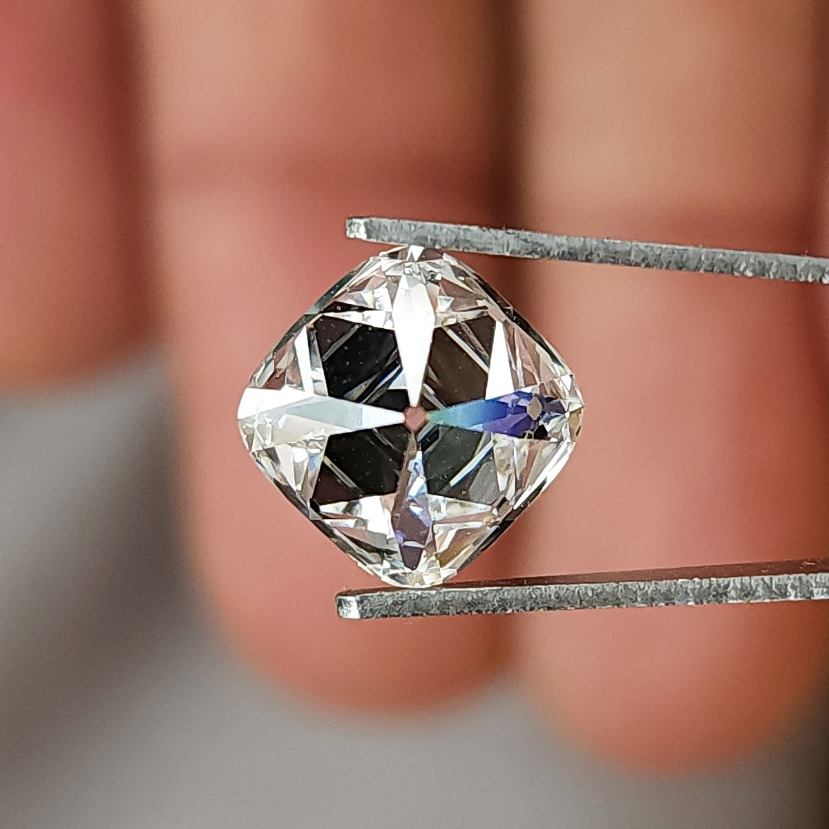 Square cushion cut diamond held in tweezers showing small spectral flare on pavilion facets.