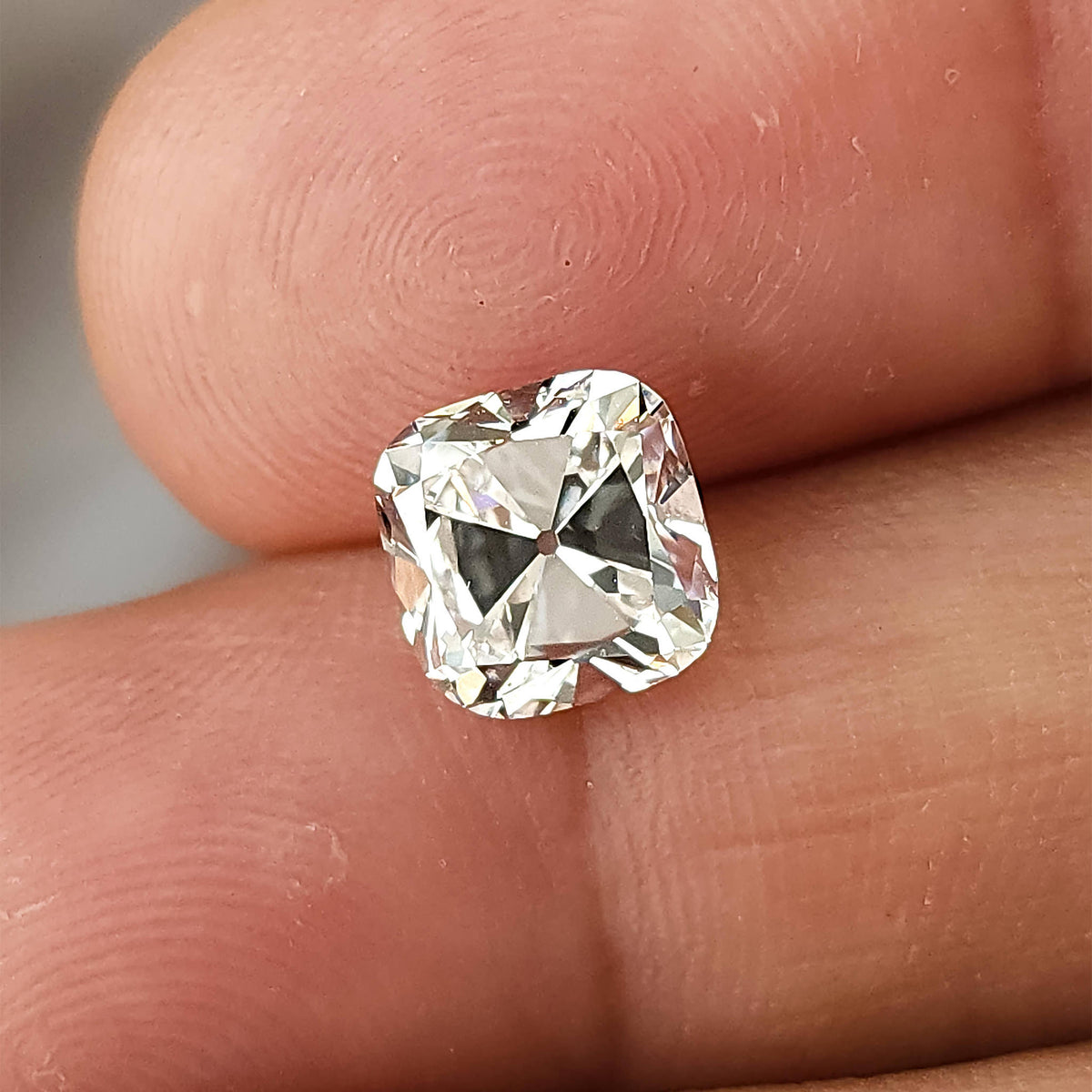 Colorless square cushion cut gem resting between fingertips providing a human scale reference.