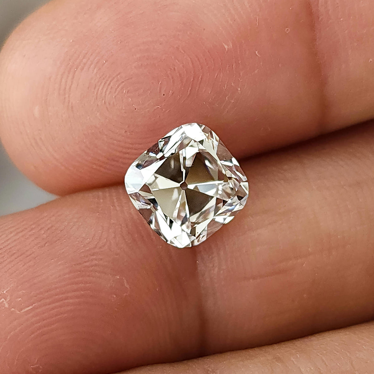 Close-up of square cushion cut stone held between fingers under soft natural light.