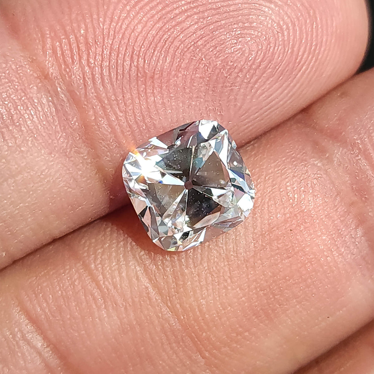 Tilted square cushion cut gem held in hand, showing surface brilliance and antique style faceting.