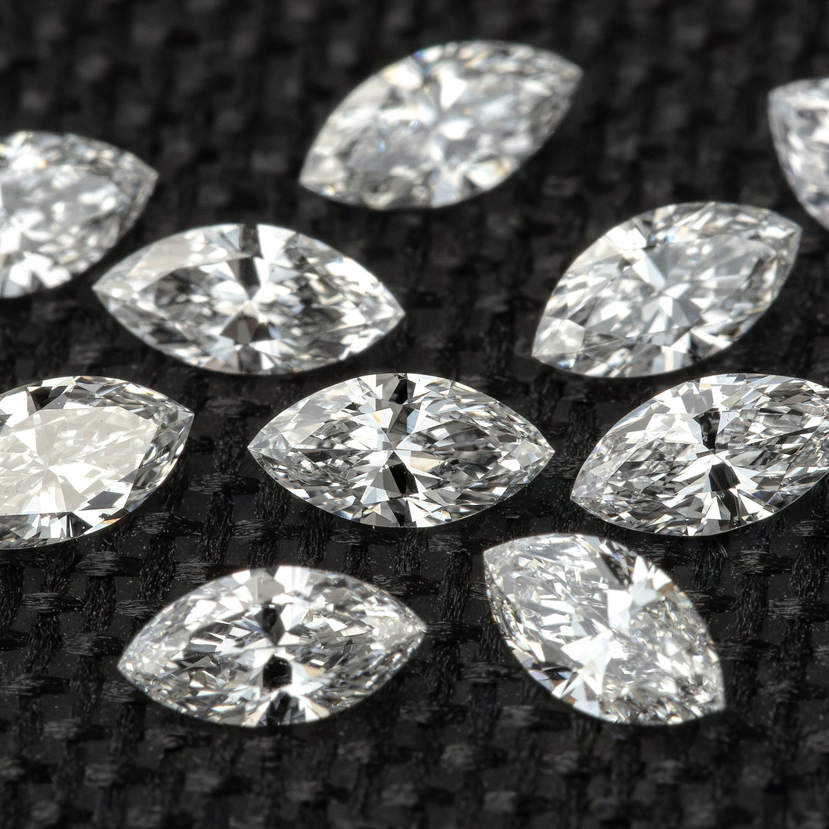 Marquise diamond parcel photographed at a low angle, with sparkling foreground facets against dark fabric.