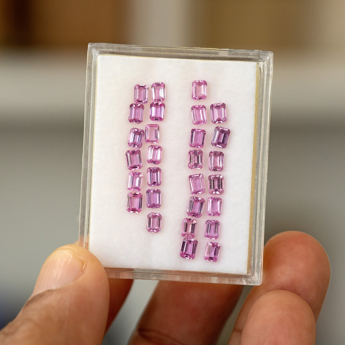 Hand-held tray of representative pink emerald-cut sapphires, tilted slightly to show their rectangular stepped outlines and reflections.