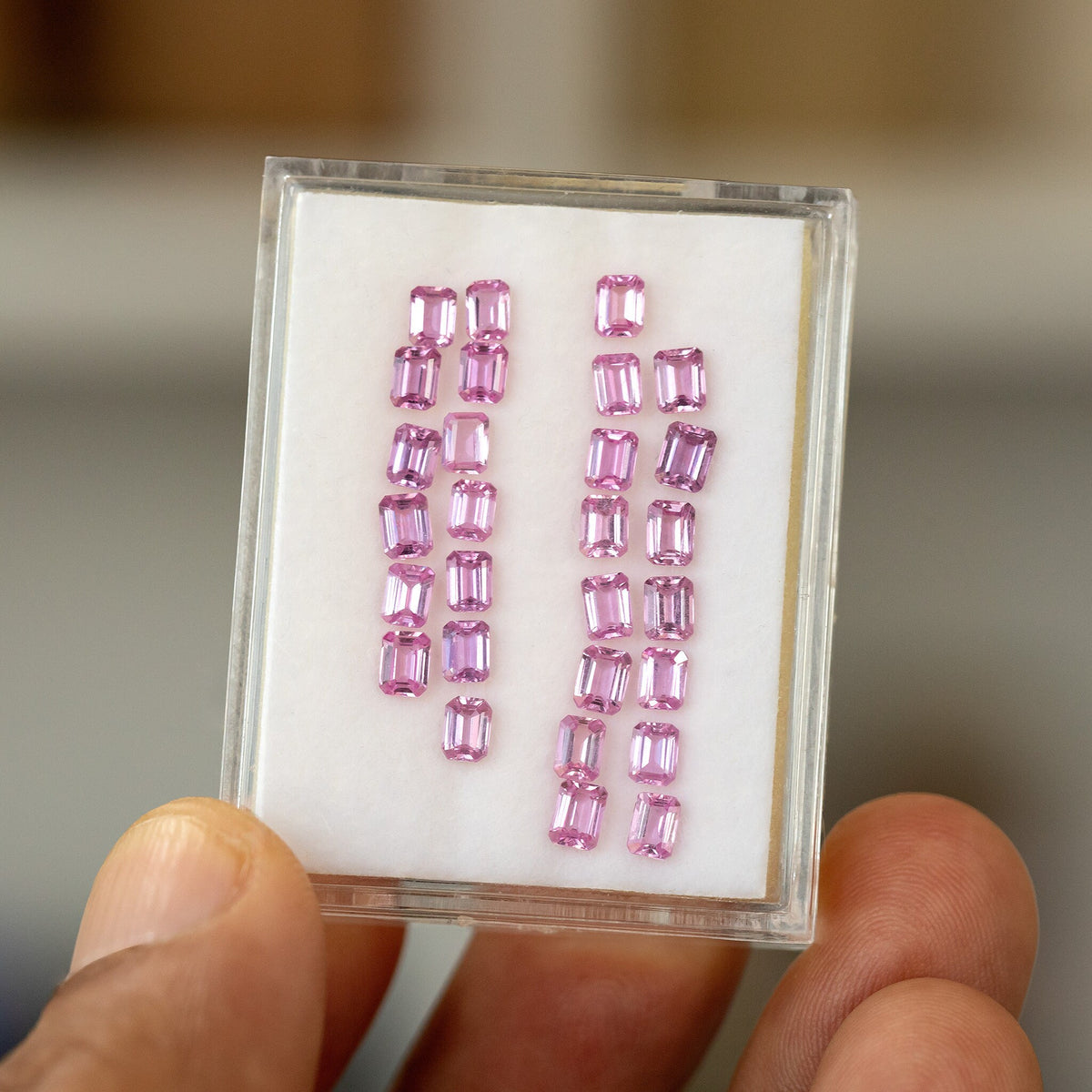 Full representative parcel of pink emerald-cut sapphires in a hand-held white display tray; one random sapphire is supplied per purchase.