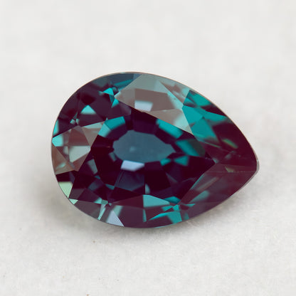 Crown-facing pear lab-grown alexandrite sample on a pale surface, with blue-green and reddish reflections.