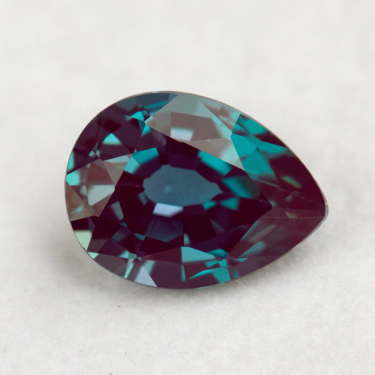 Crown-facing pear lab-grown alexandrite sample on a pale surface, with blue-green and reddish reflections.