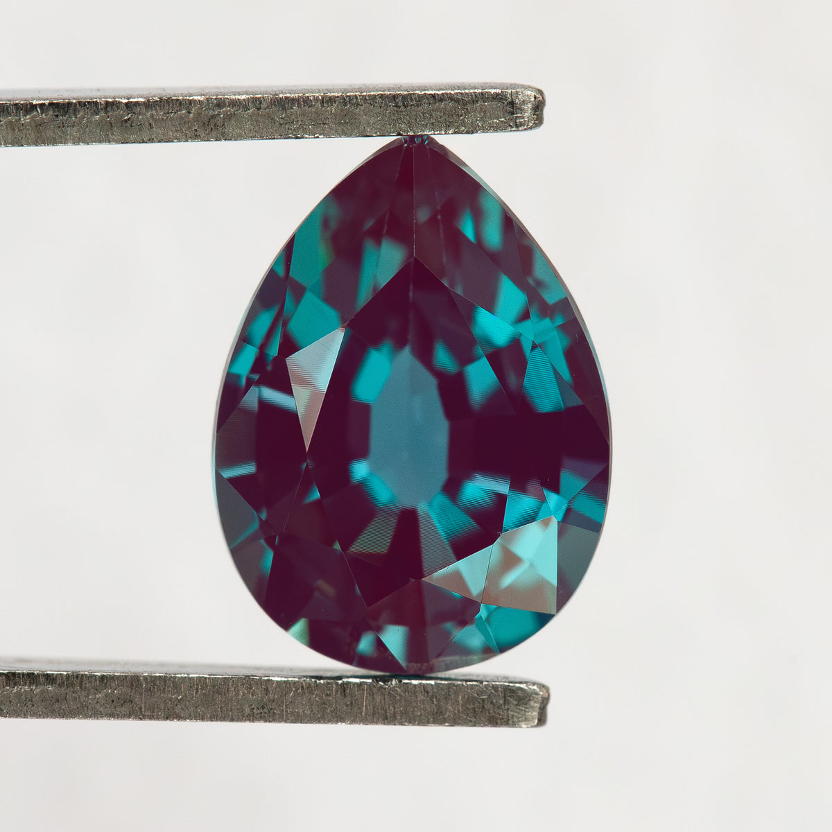 Pear sample held upright in tweezers, with the pointed end at the top and crown facets visible.