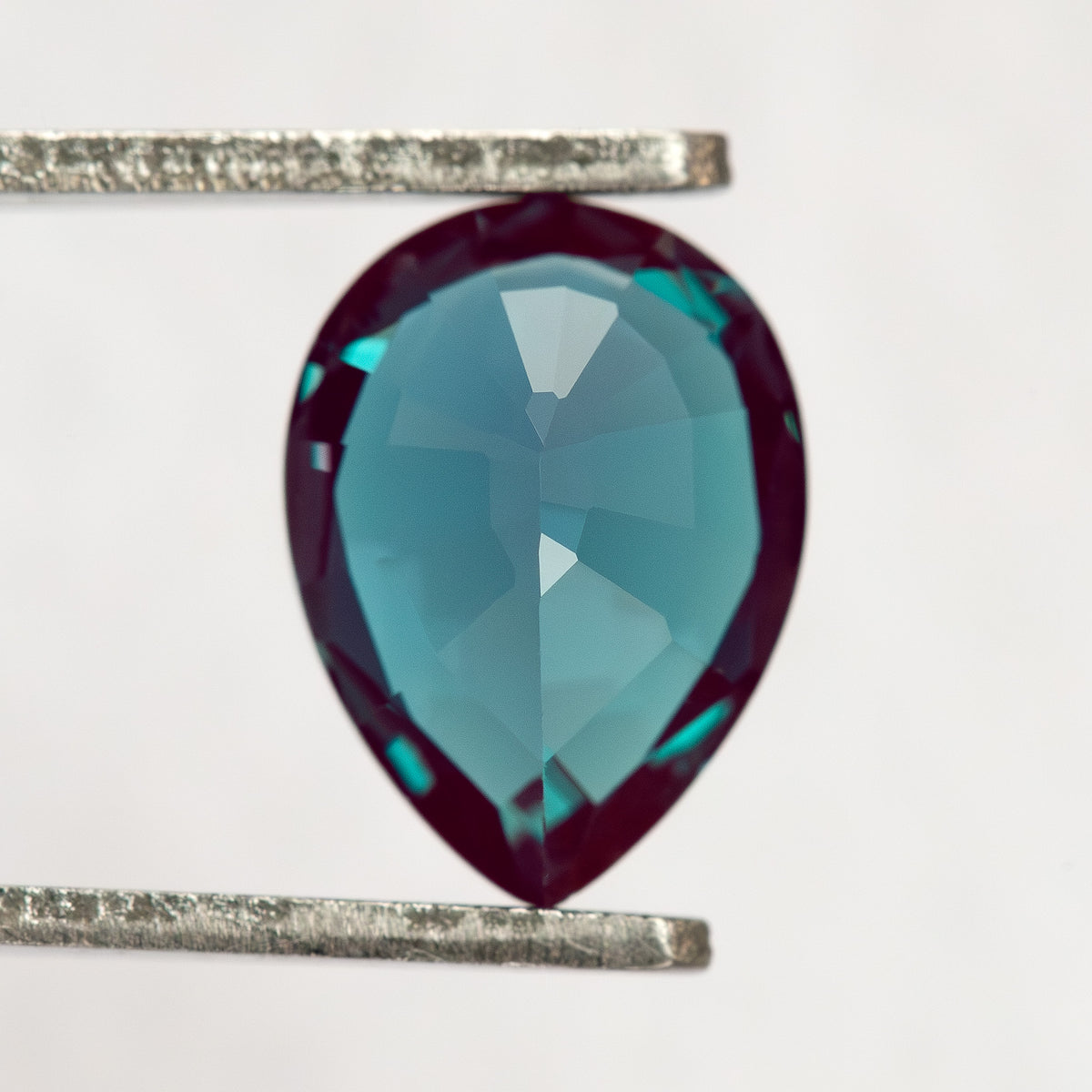 Pavilion-facing pear sample in tweezers, showing the back facets rather than the face-up crown.