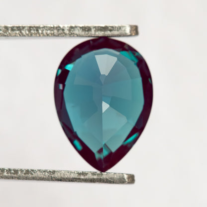 Pavilion-facing pear sample in tweezers, showing the back facets rather than the face-up crown.