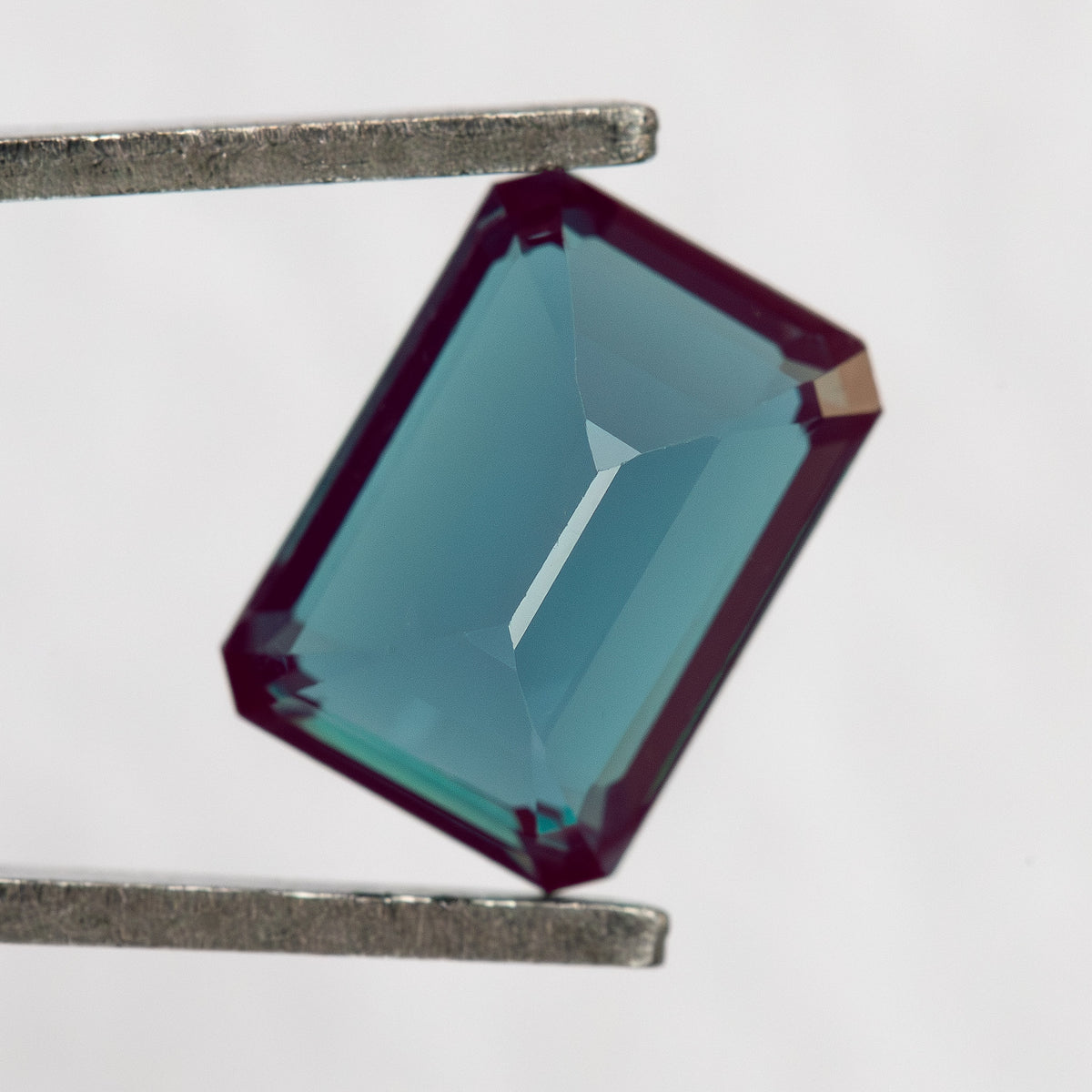 Pavilion-facing rectangular sample in tweezers, showing the back facet structure.