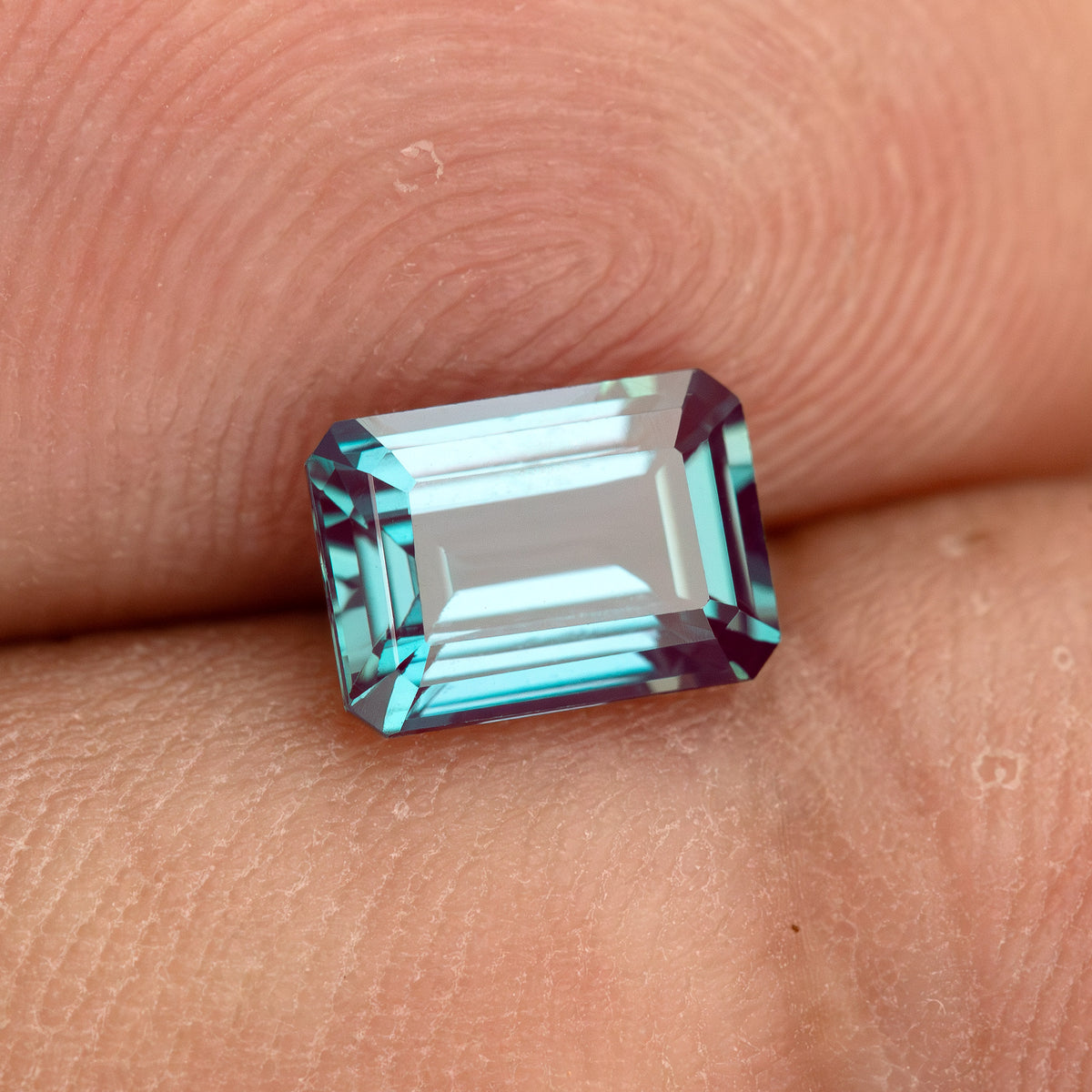 Emerald-cut sample on fingertips, providing scale context for the calibrated design.
