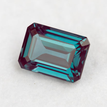Crown-facing emerald-cut lab-grown alexandrite sample on a pale surface, showing its rectangular step pattern.