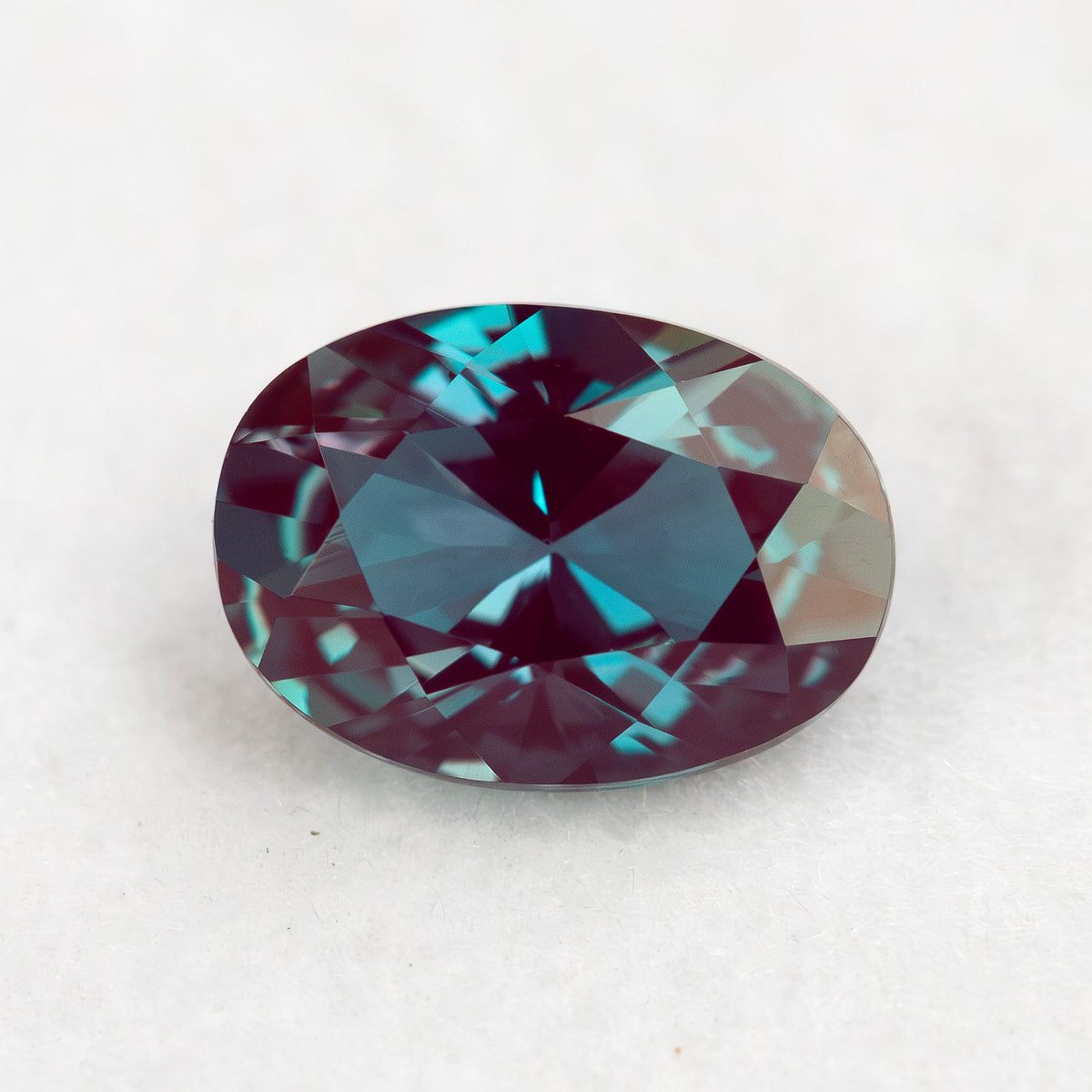 Crown-facing oval lab-grown alexandrite sample on a pale surface, showing blue-green and reddish reflections.