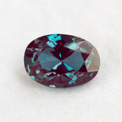 Crown-facing oval lab-grown alexandrite sample on a pale surface, showing blue-green and reddish reflections.