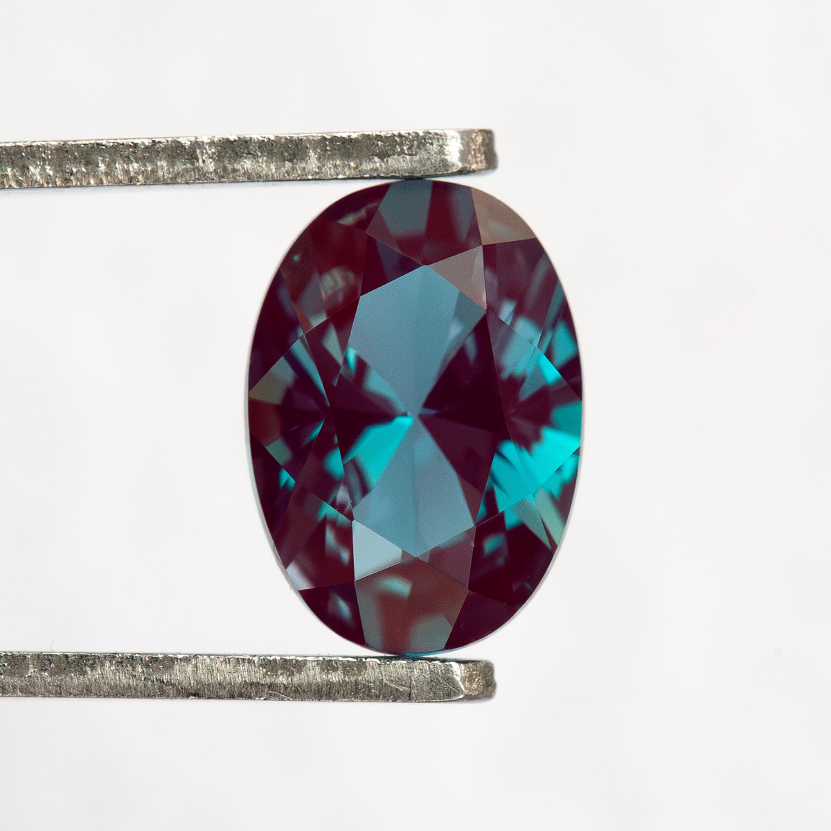 Oval sample held upright in tweezers, with its crown facing the viewer.