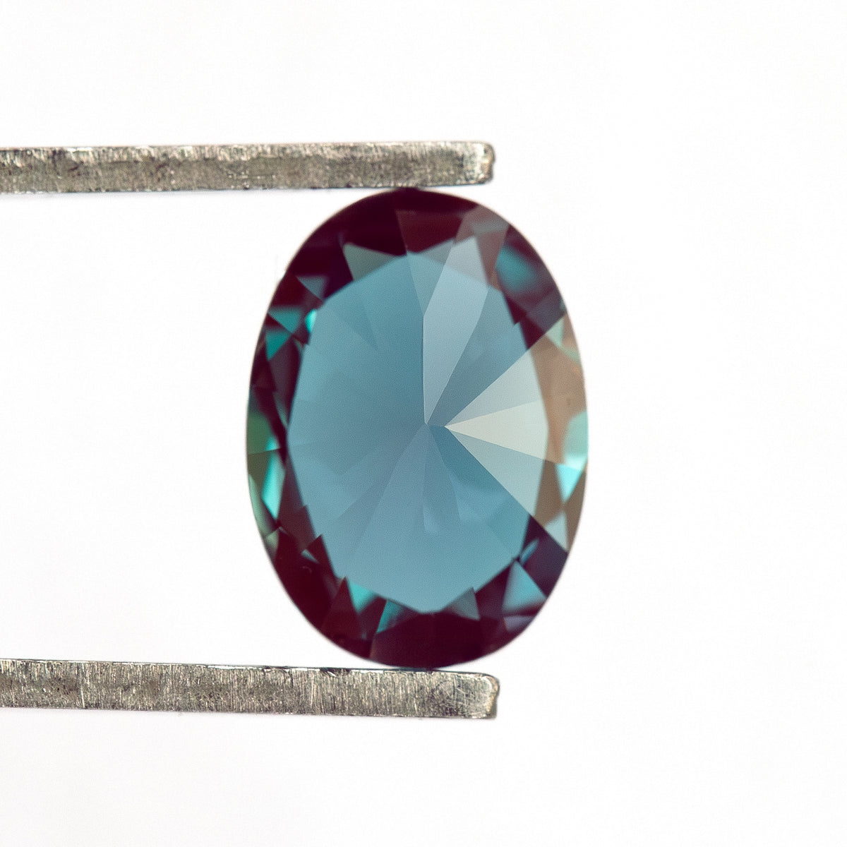 Pavilion-facing oval sample in tweezers, showing the back facets.