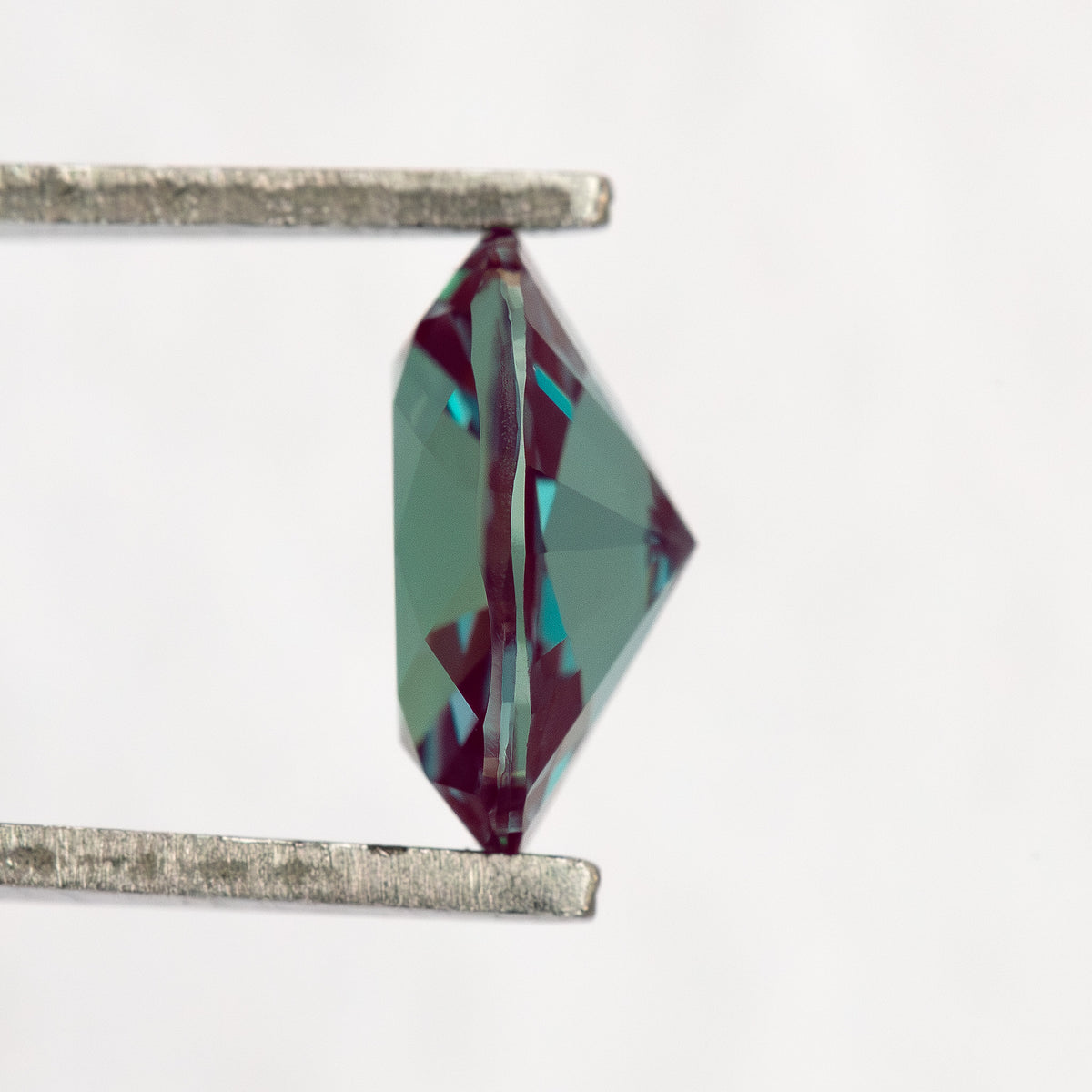 Side profile of the oval sample between tweezers, showing crown and pavilion depth.