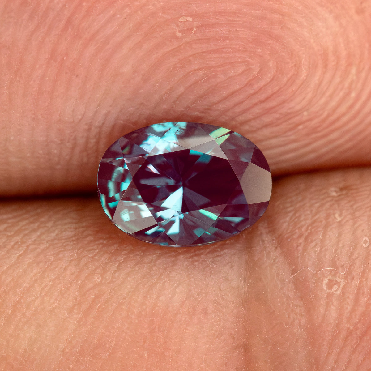 Second fingertip view of the oval sample, with its table and crown facets visible.