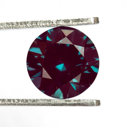 Crown-facing round lab-grown alexandrite sample held in tweezers, showing its circular outline.
