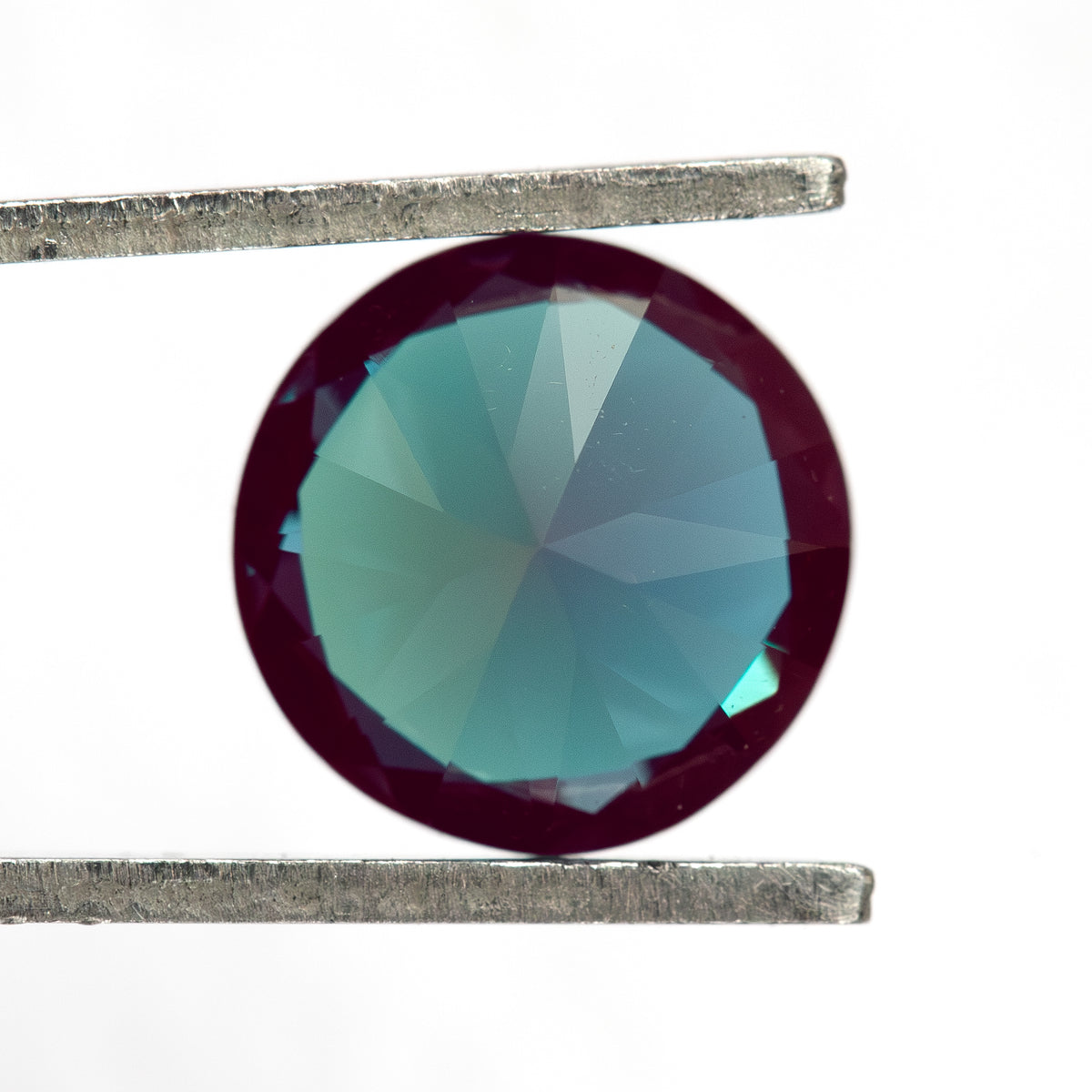 Pavilion-facing round sample in tweezers, showing its back facet pattern.