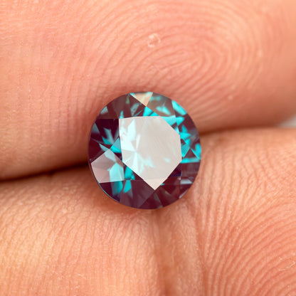 Tilted round sample on fingertips with a pale reflection across its table.